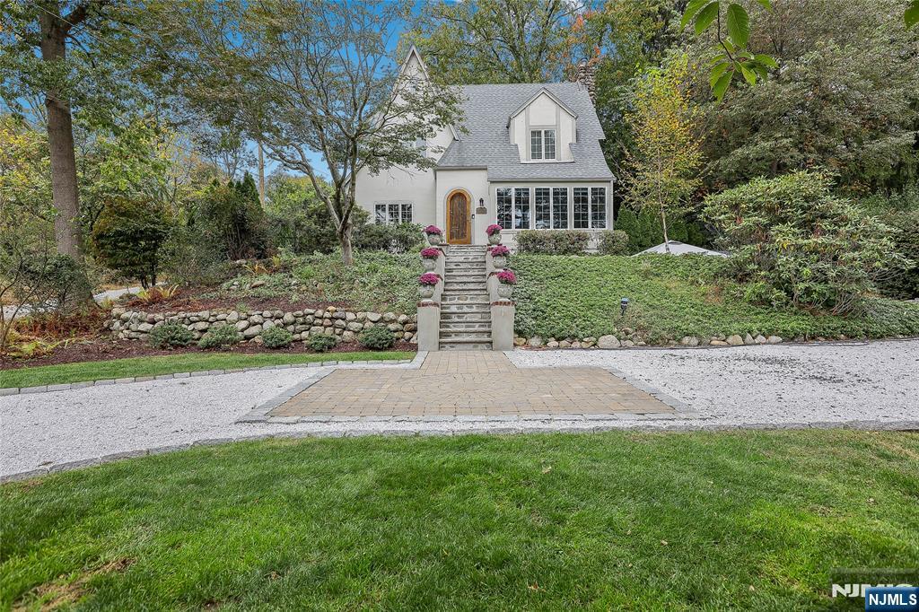 Full of charm and warmth, this beautifully updated French Tudor in the heart of Ramsey blends timeless appeal with modern comfort. Set on a tiered property with a circular driveway, lush greenery, and professional lighting in the front, side, and back yards, this early 1900s home welcomes you with its graceful stucco facade and storybook style. Inside, hardwood floors, a cozy living room with a gas fireplace, and French doors opening to a peaceful garden create an inviting atmosphere. The bright sunroom, framed by new Andersen windows and its own French door, is the perfect place to relax. A formal dining room flows into the renovated 2021 kitchen featuring quartzite countertops, stainless steel appliances, and ample cabinet space. Upstairs are three comfortable bedrooms and a stylish full bath renovated in 2023. The third floor offers flexible space for an office, studio, or extra bedroom with backyard views. The finished basement includes a second fireplace, laundry, storage, and potential for another bath. Outdoors, enjoy a large stone patio with fireplace, an upper yard with fire pit and seating, and a hidden â€œsecret gardenâ€ with fruit trees, a grapevine-covered gazebo, and a charming she-shed/greenhouse with half bath. Recent updates include new plumbing, electric, Andersen windows, and a newer roof. With a circular driveway, attached garage, and proximity to Finch Park, downtown Ramsey, and shopping, this home perfectly combines privacy, comfort, and timeless charm.